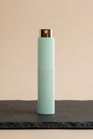 Reise-Flakon 10 ml mit mintfarbener Hülse und Goldpumpe, stehend auf dunkler Schieferplatte